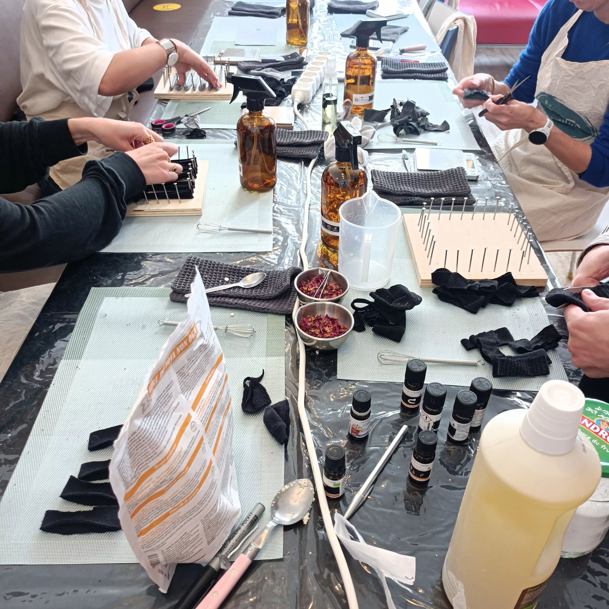 Une table avec des produits ménagers à fabriquer, des personnes autour. Il s'agit d'un team-building DIY en entreprise.