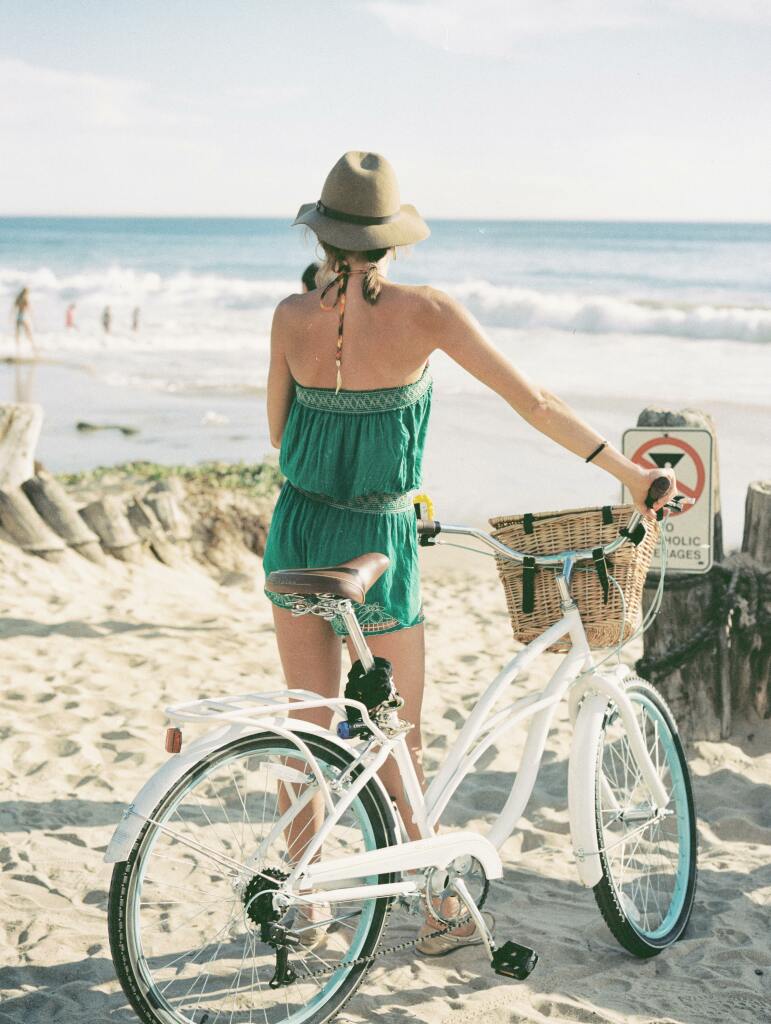 Une dame tient son vélo à la plage.