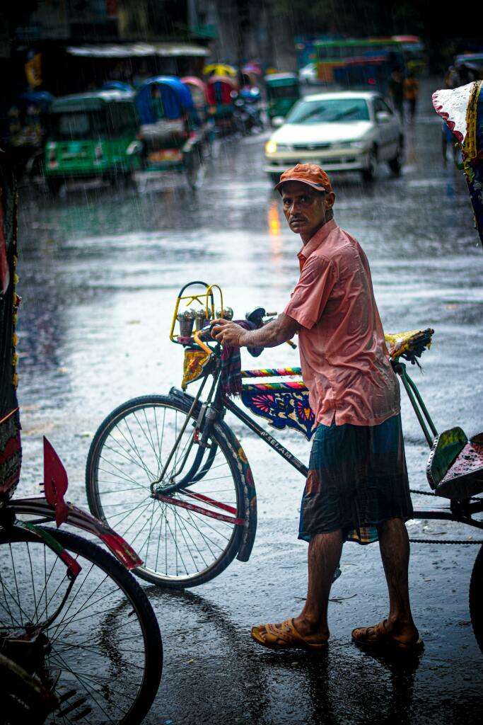 Un monsieur tient son vélo sous la pluie, il est trempé.