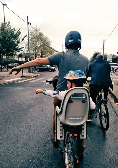 Un papa et son enfant sur un vélo. Ils tendent le bras pour tourner.