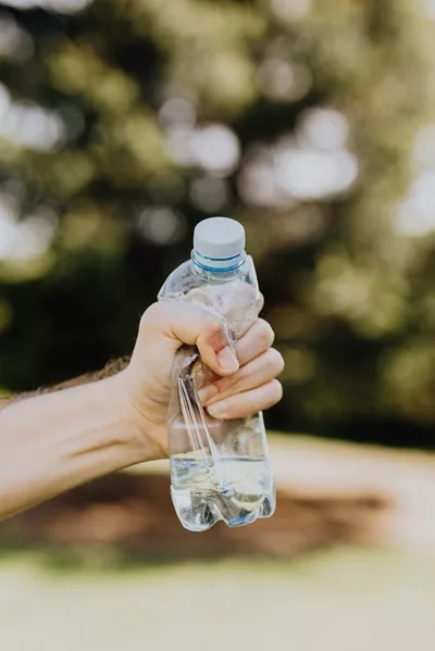 une main écrase une bouteille plastique. Elle montre qu'il faut réduire les déchets et le plastique à usage unique.